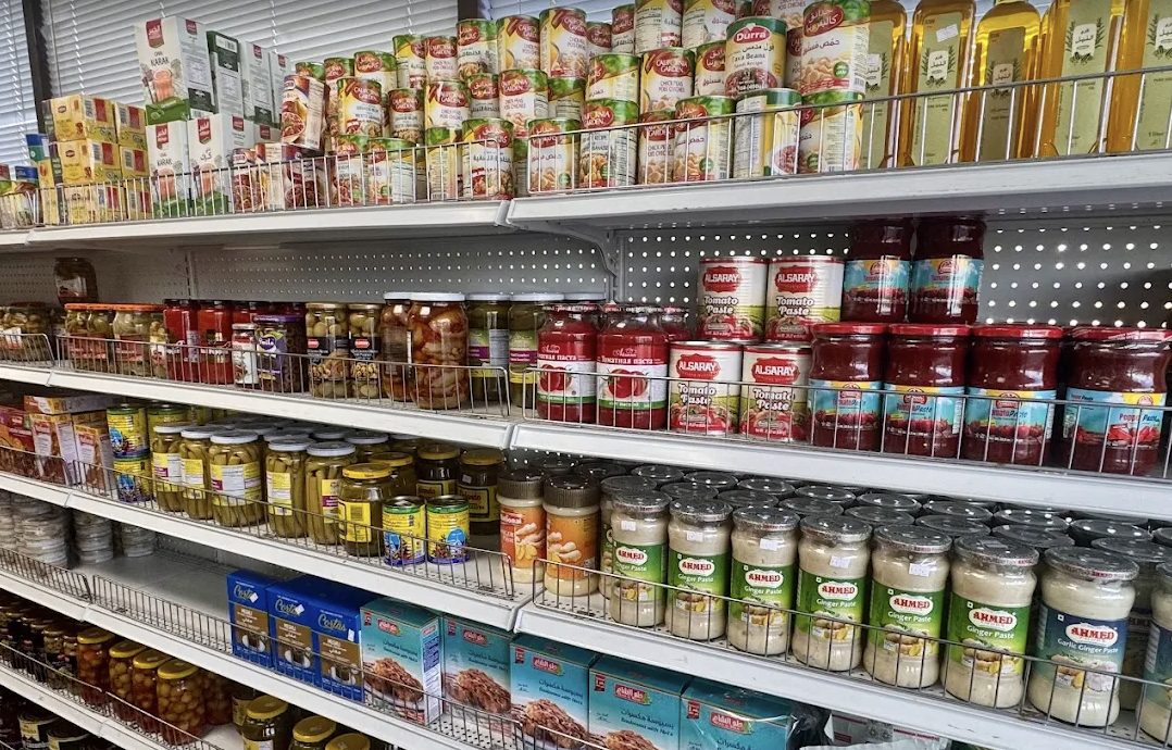 Fully stocked shelves inside Halal Bangla Grocery with canned goods, pickles, tomato paste, and cooking pastes